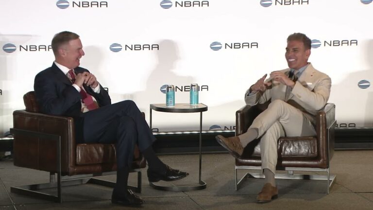 Kenn sits across someone addressing an unseen crowd at his NBAA keynote speech